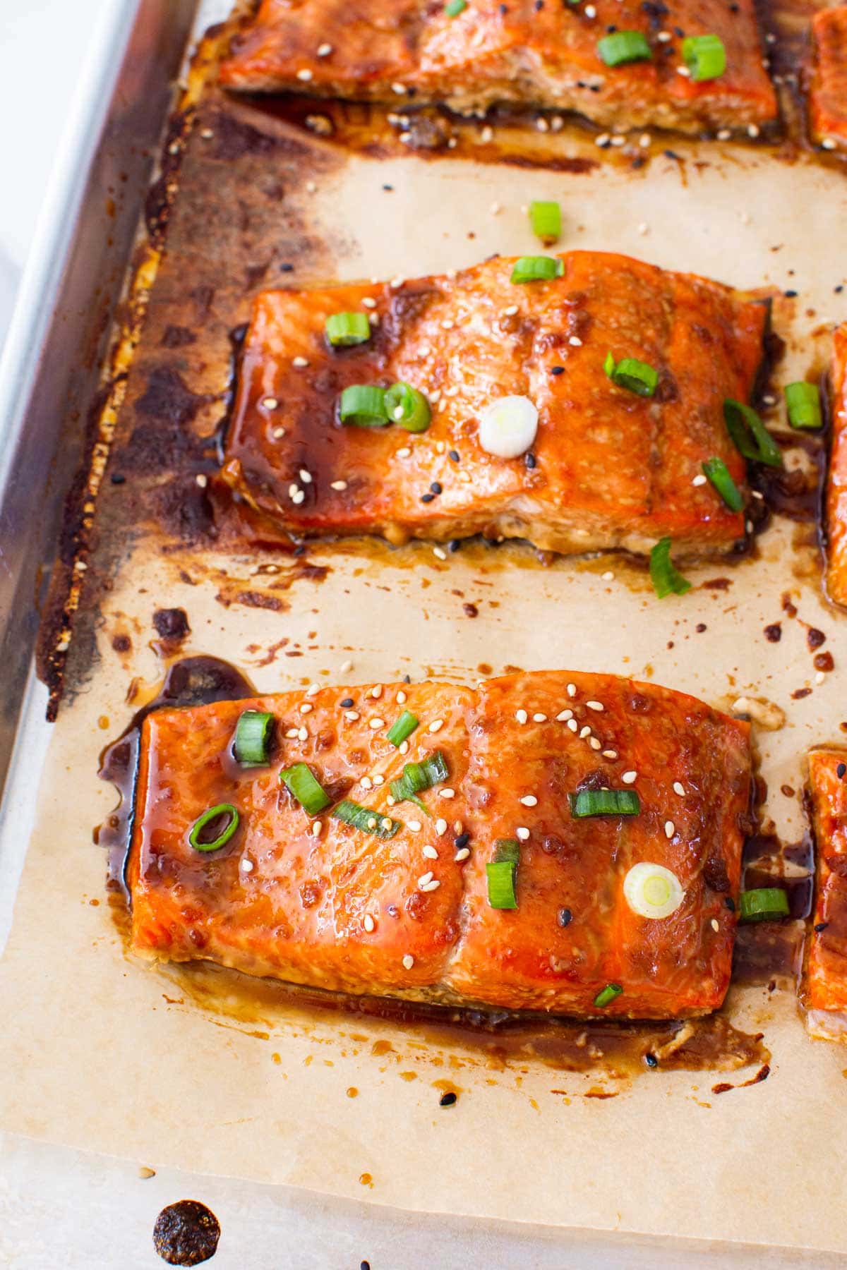 Baked salmon garnished with sesame and scallions on a baking sheet.
