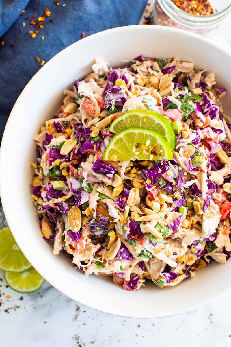 Thai chicken salad recipe served in white bowl and blue towel nearby.