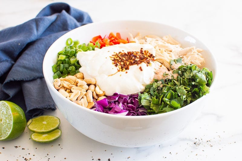 Shredded chicken, bell pepper, green onion, peanuts, cabbage, cilantro, yogurt and seasonings in white bowl.