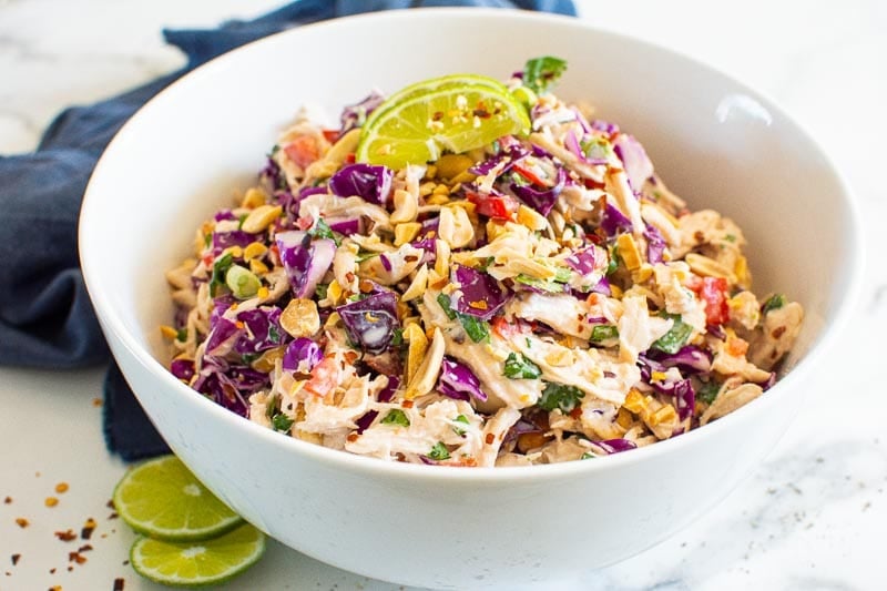 Thai chicken salad garnished with lime and hot pepper flakes in a bowl.