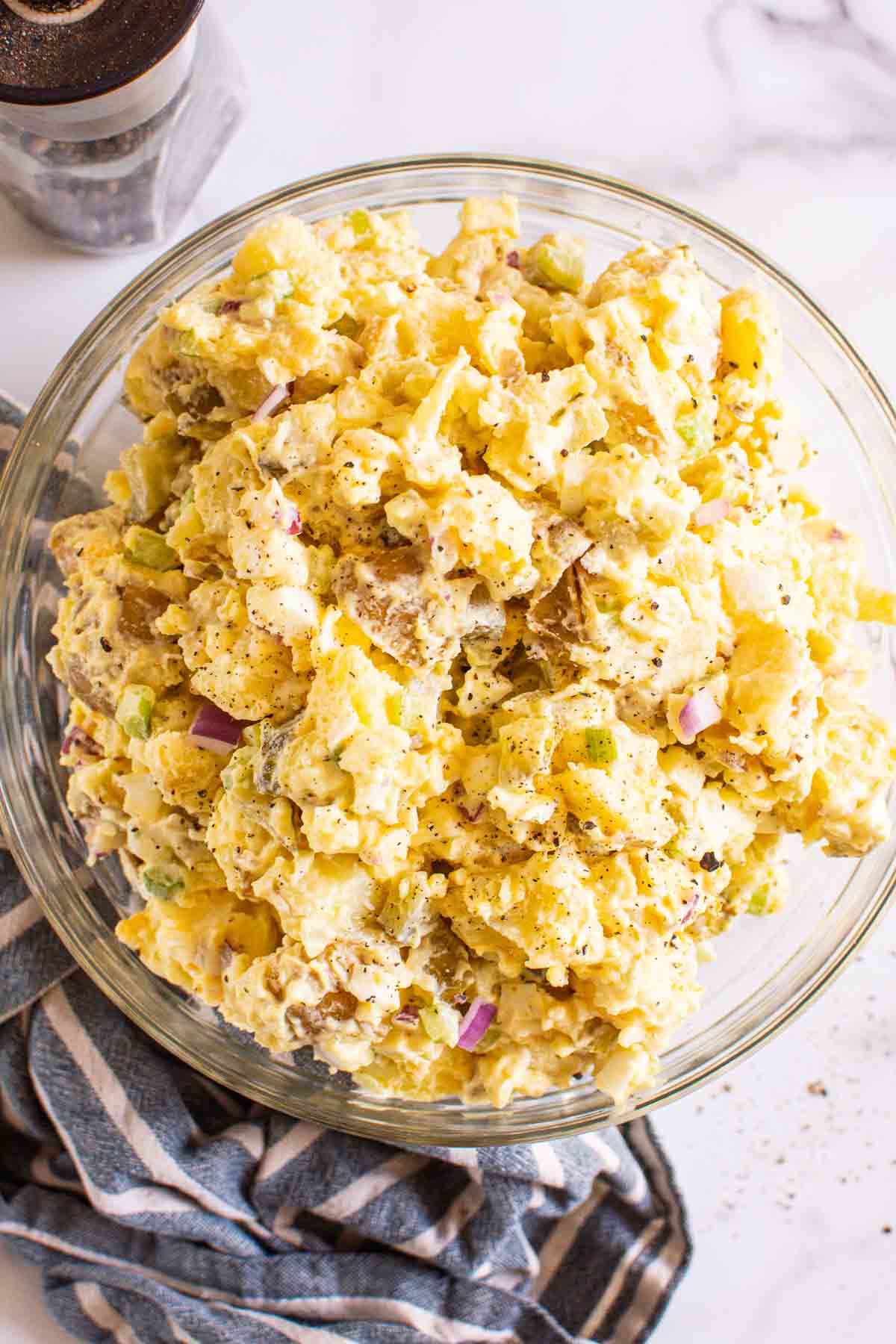 Instant Pot potato salad served in glass bowl and pepper mill behind on a counter.