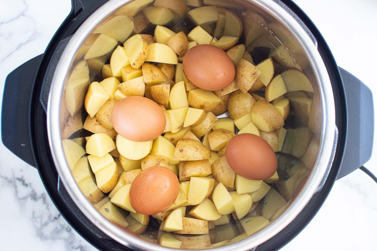 Chopped potatoes and whole eggs on top of them inside Instant Pot.