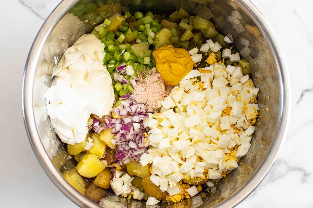 Cooked potatoes, chopped red onion, pickles, celery, eggs, yogurt, mayo and seasonings in the stainless steel pot.
