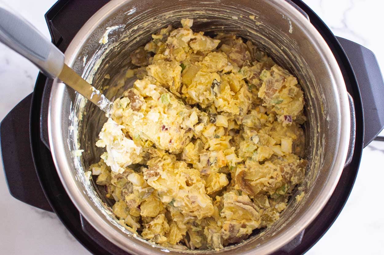 Stirred potato salad with a metal spoon right inside the pressure cooker.