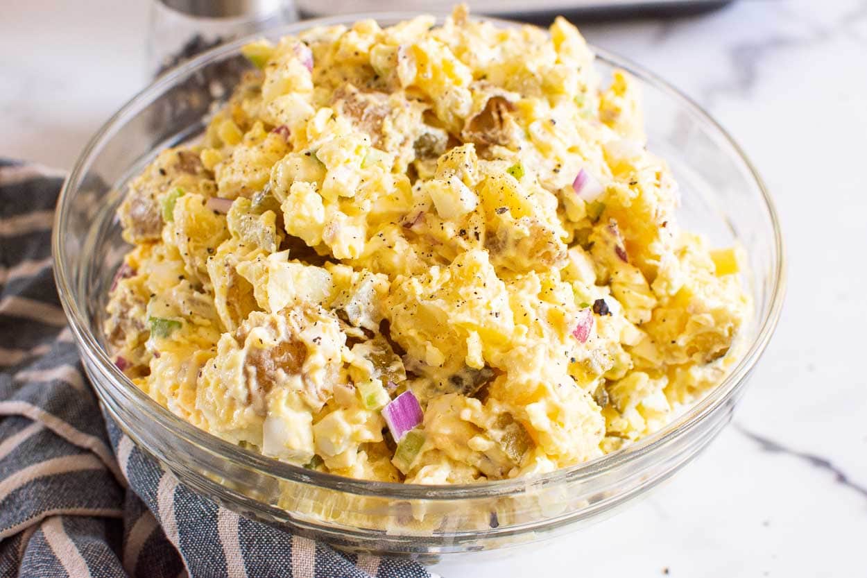 Instant Pot potato salad served in glass bowl and pepper mill and towel on a counter.