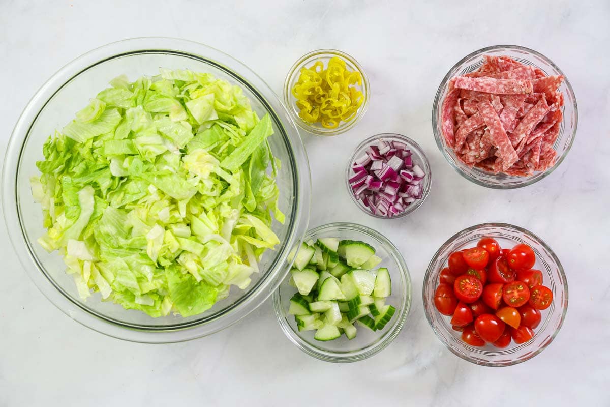 Chopped lettuce, vegetables and salami in bowls.