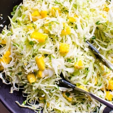 Mango slaw served in a black bowl with tongs.