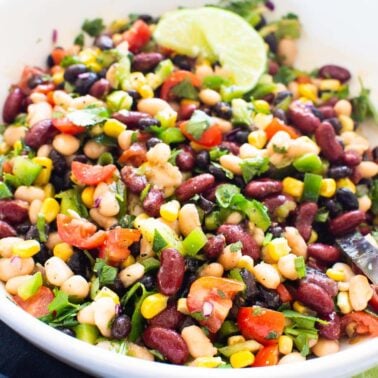 Mexican bean salad with corn, tomato, cilantro and garnished with lime in white bowl.