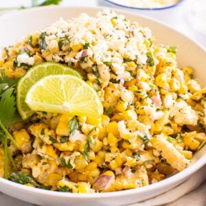 Mexican street corn salad in a bowl with lime slices.
