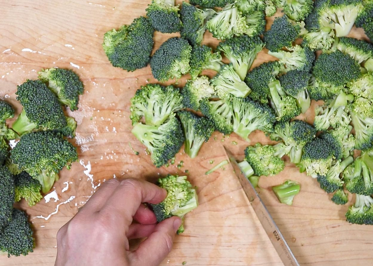 Chopping broccoli florets into bite-sized pieces on a cutting board.