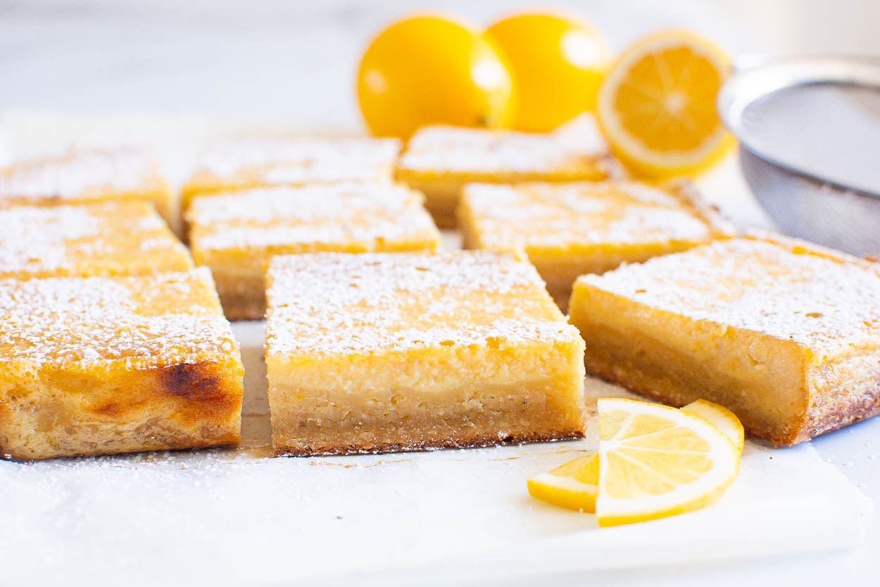 Healthy lemon bars, sliced and whole lemons and a sieve with icing sugar.