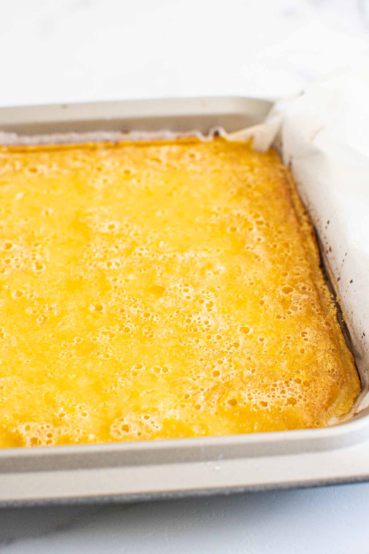 Baked lemon bars in a baking dish lined with parchment paper.