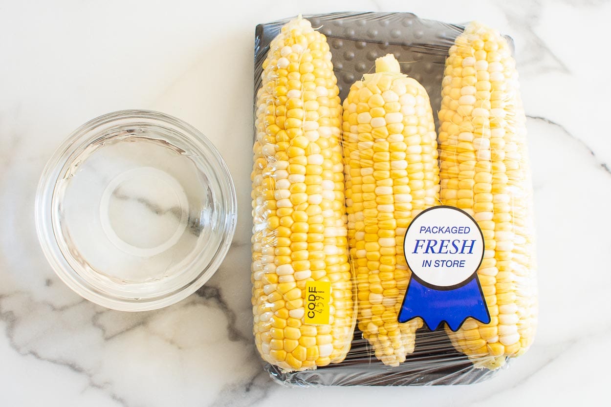 Three ears of corn in a package and a bowl with water.