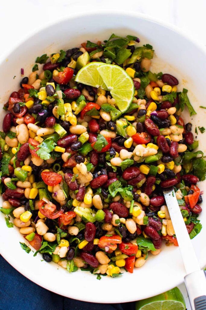 mexican bean salad in white bowl with metal spoon