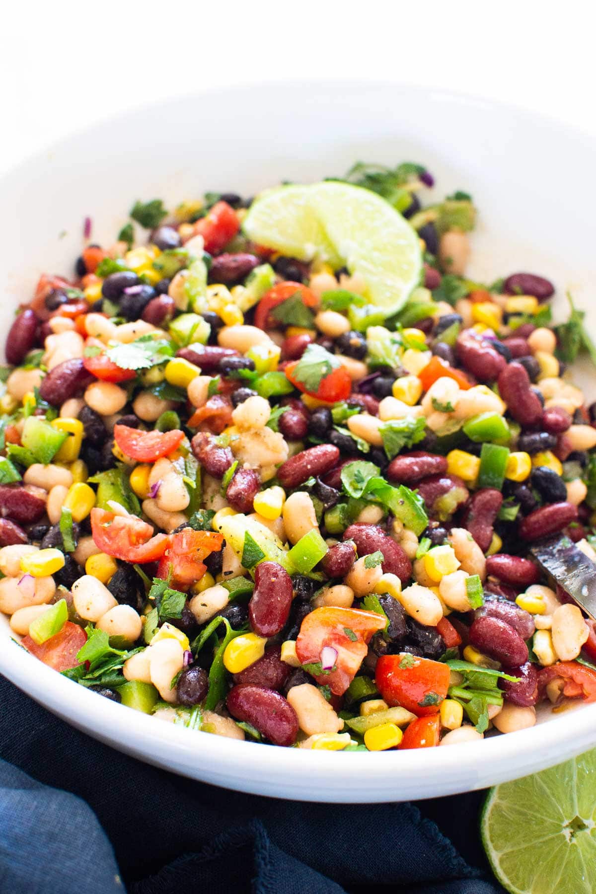 Mexican bean salad with corn, tomato, cilantro and garnished with lime in white bowl.