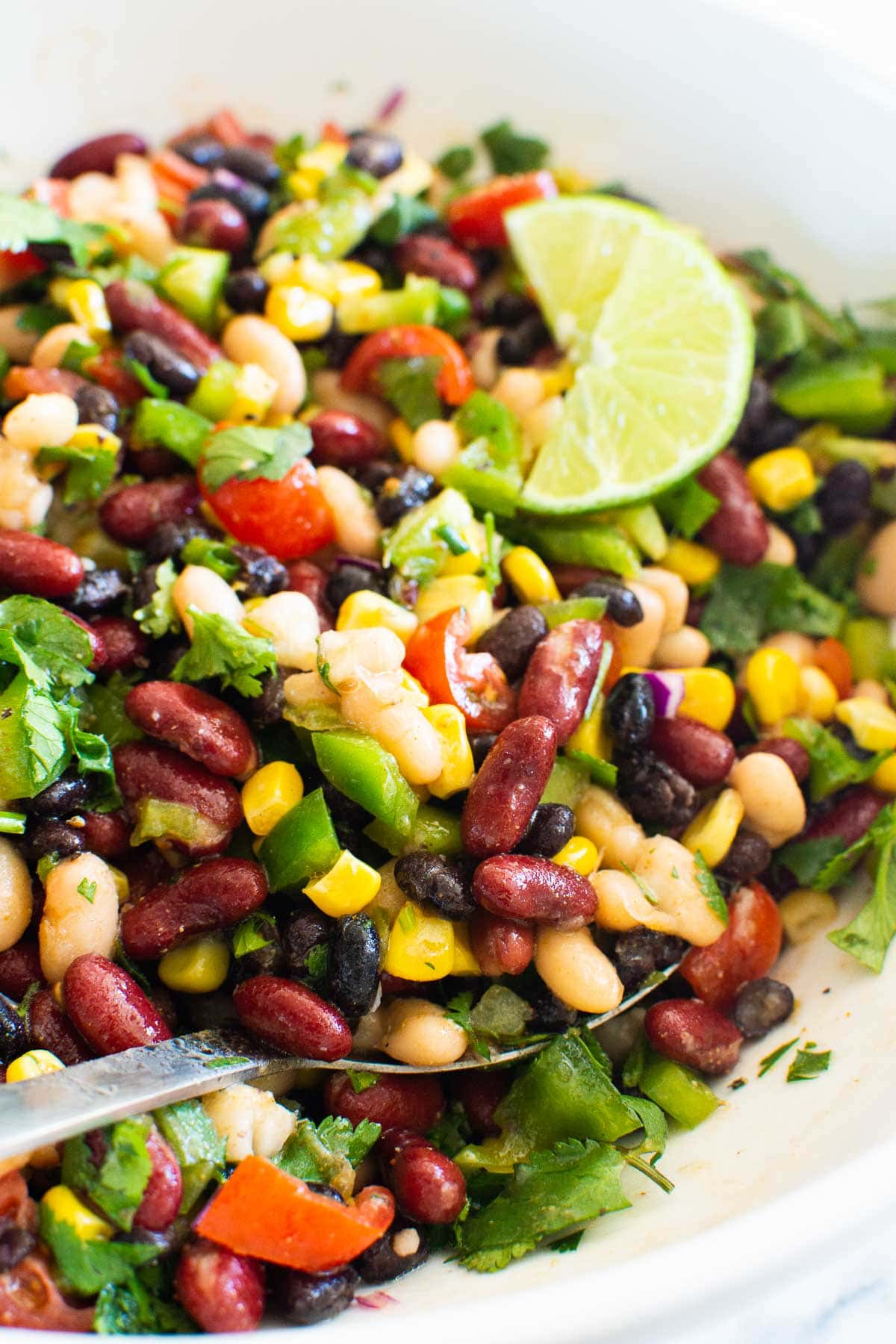 Mexican bean salad on a metal spoon garnished with lime in white bowl.