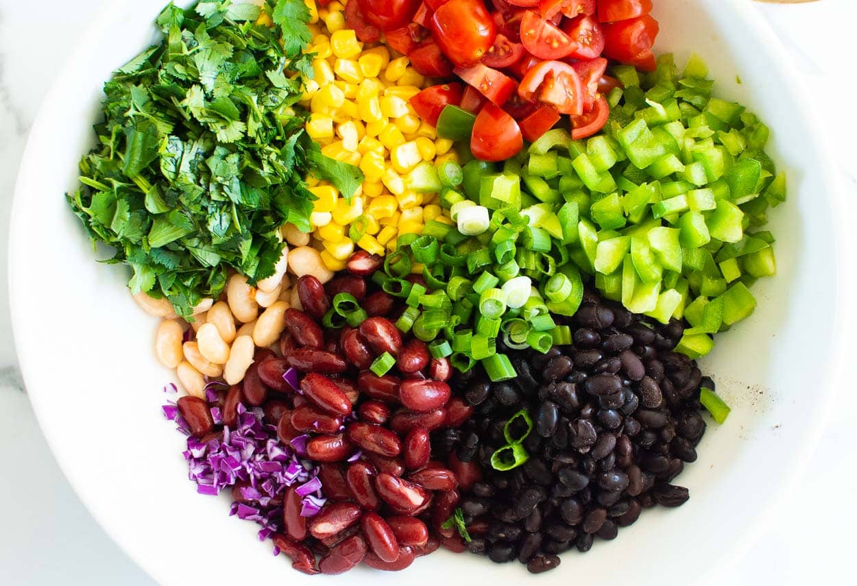 Black beans, red kidney beans, tomato, white beans, cilantro, corn, bell pepper, green onion in white bowl.