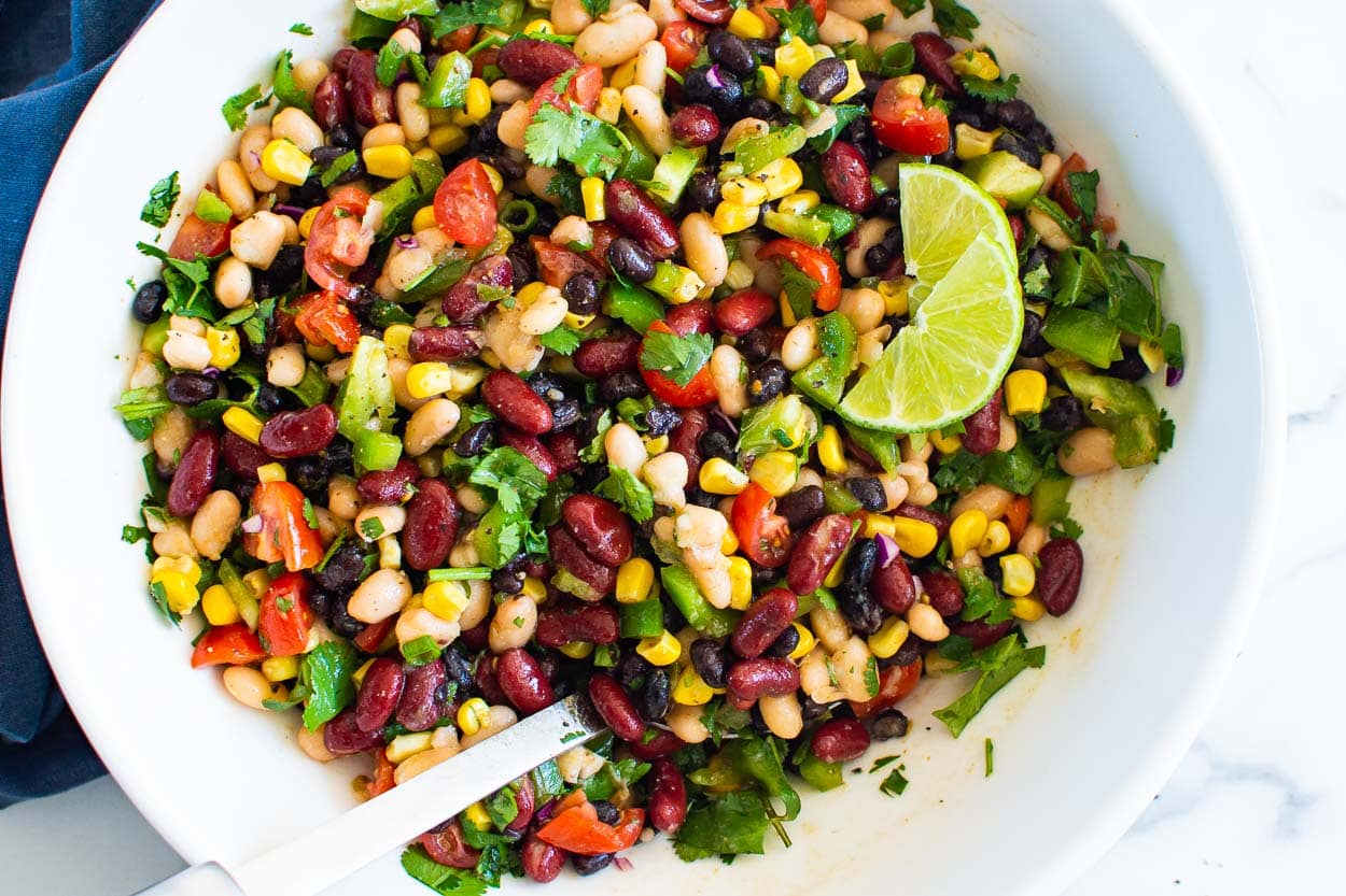 Mexican three bean salad in white bowl with lime wedges.
