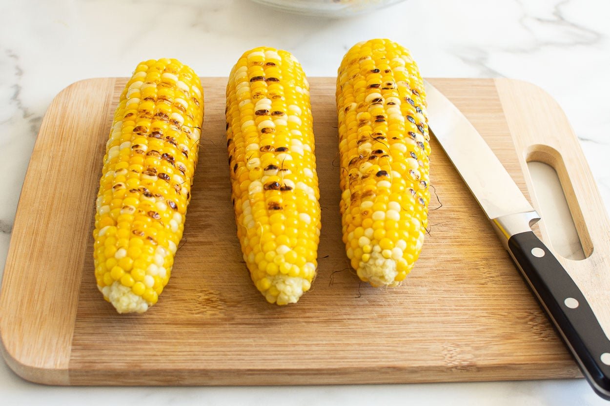 Three ears of grilled corn on a cutting board.