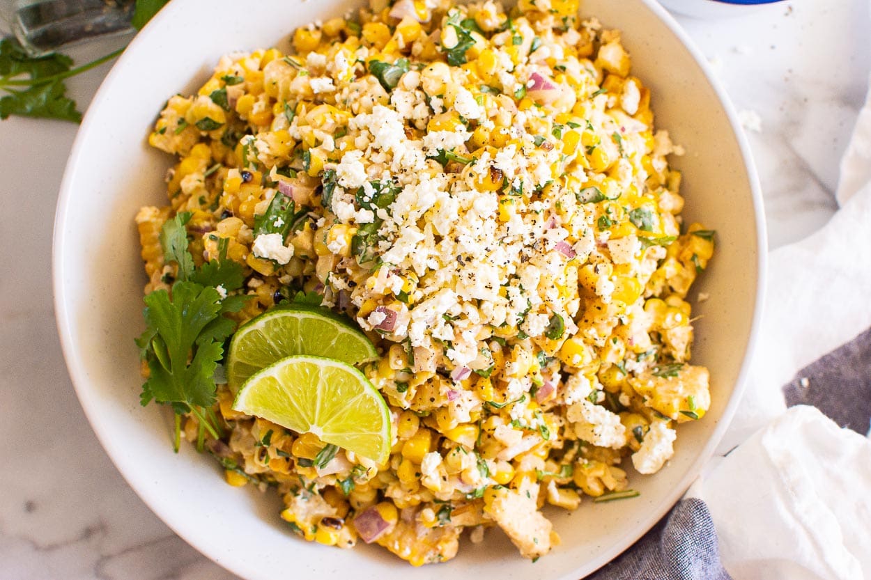 Mexican street corn salad with lime wedges and cilantro sprigs.