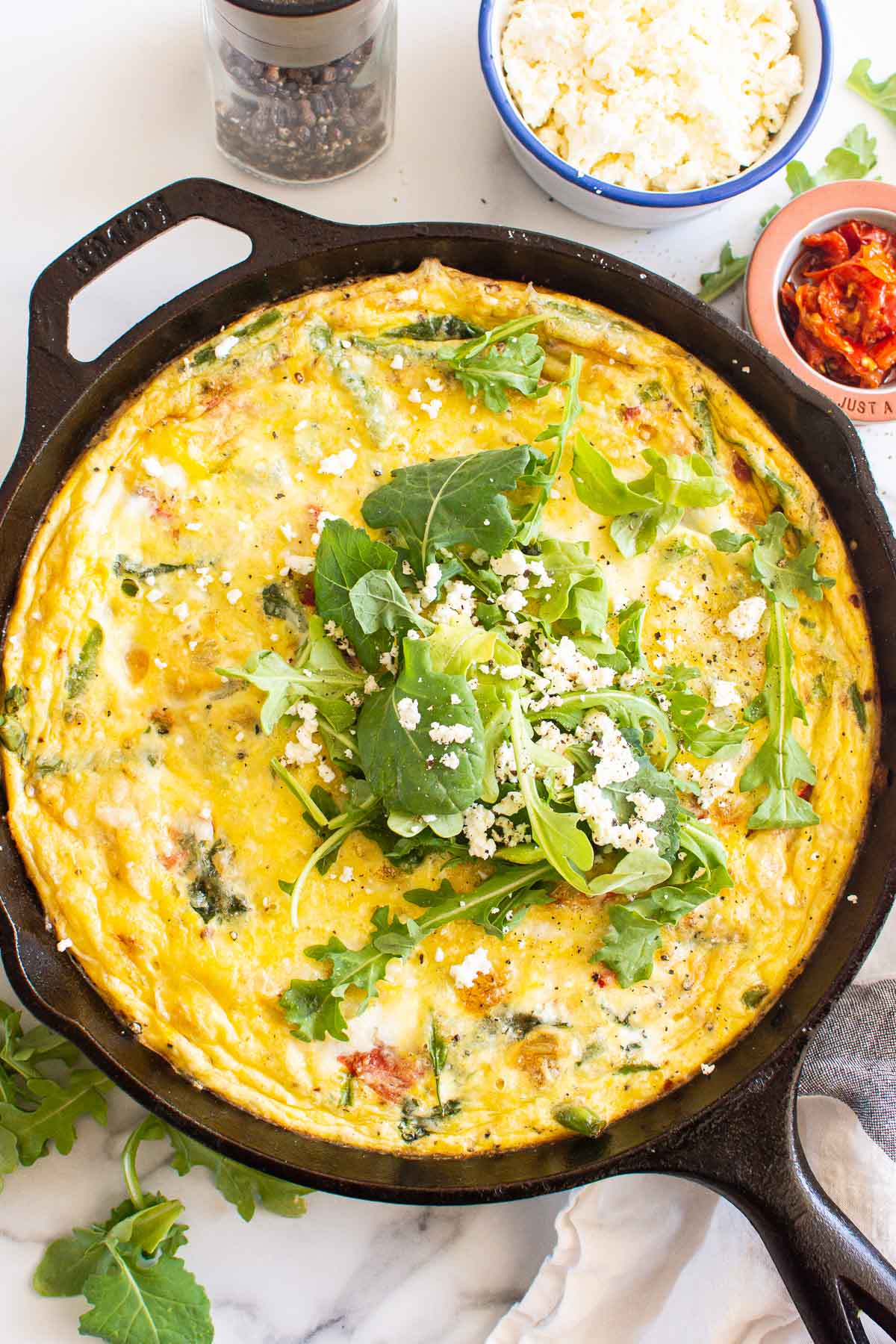 Vegetable frittata in a skillet garnished with feta cheese and greens.