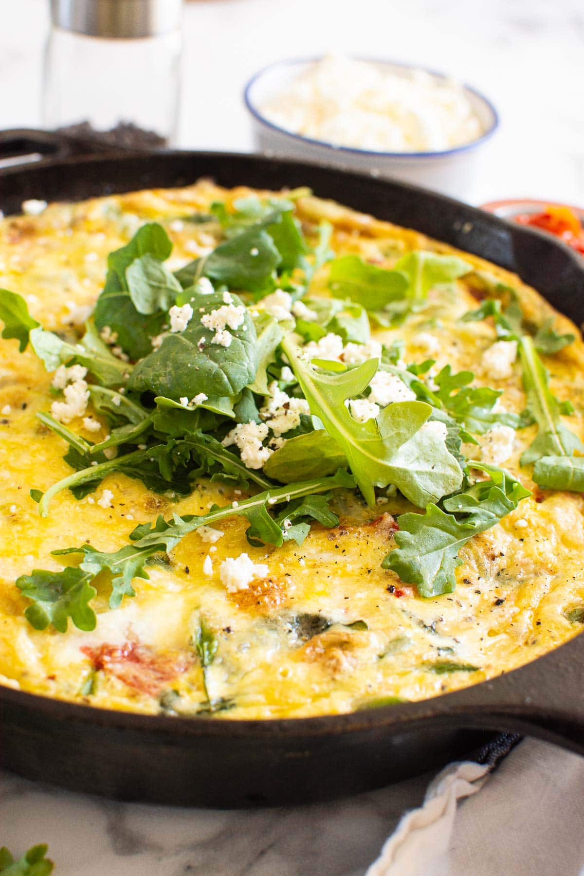 Vegetable frittata in skillet with feta and greens on top.