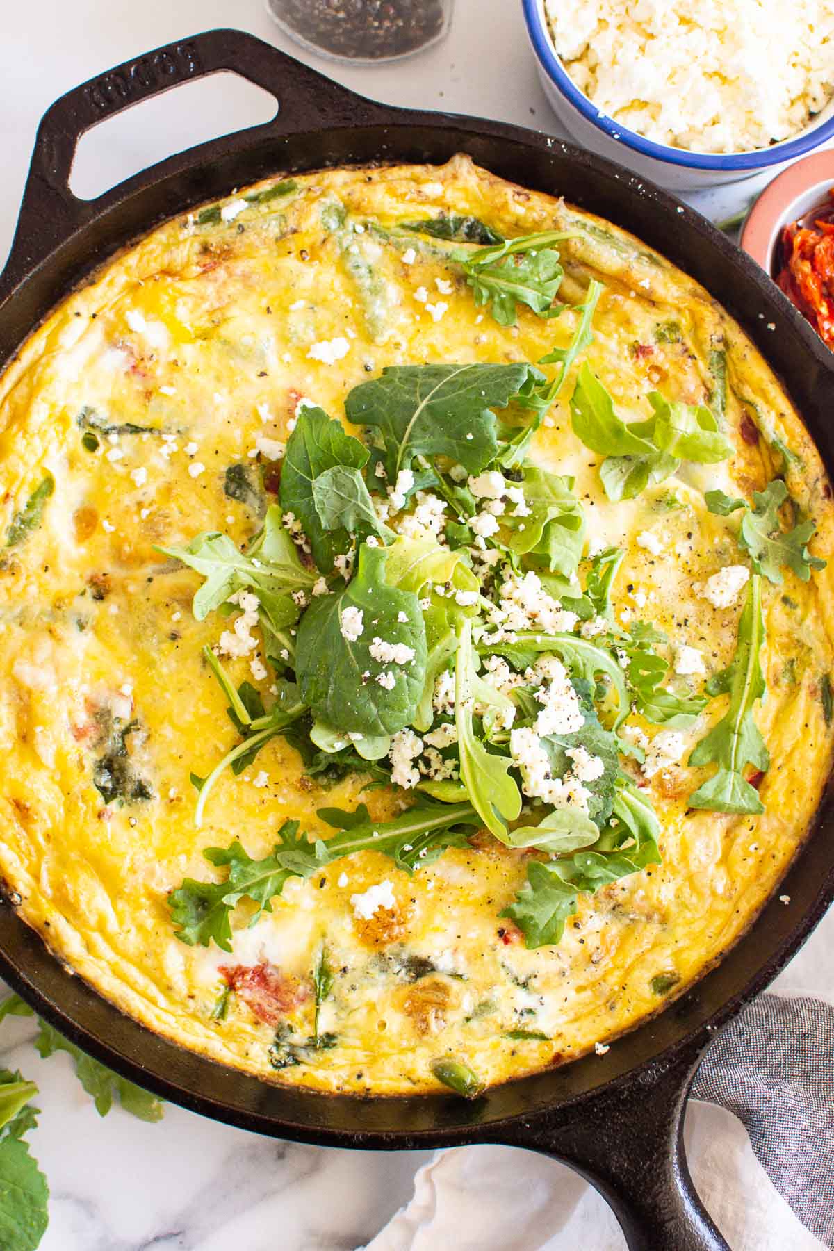 Vegetable frittata garnished with microgreens and feta in cast iron skillet.