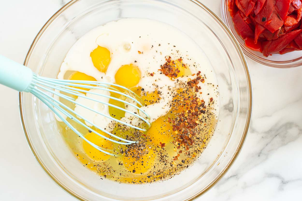 Eggs, milk, spices in glass bowl with a whisk.