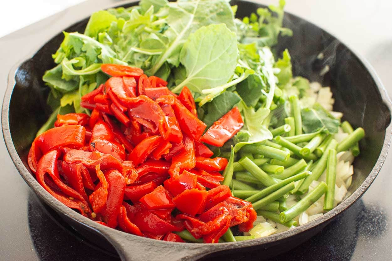 Sauteed onion, roasted red peppers, green beans, greens and onion in a skillet.