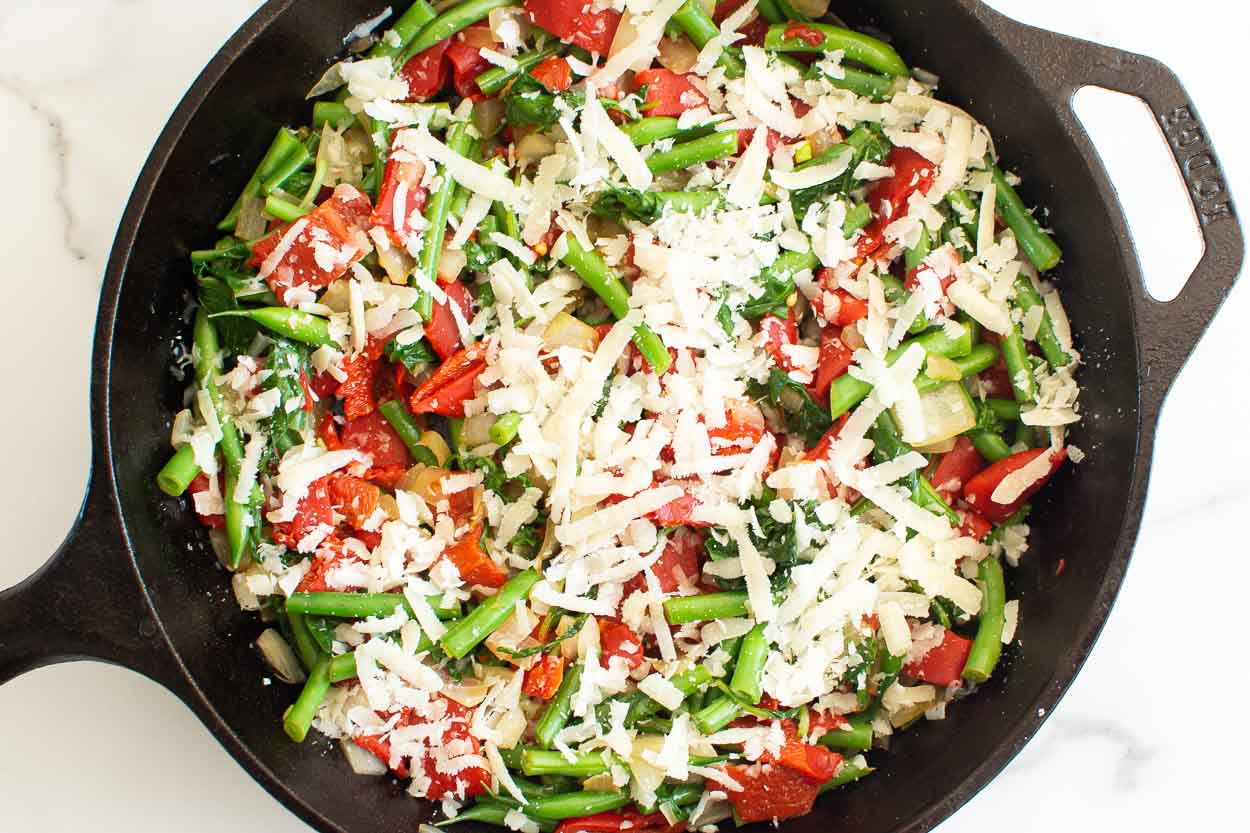 Sauteed onion, roasted red peppers, green beans sprinkled with parmesan cheese in a skillet.