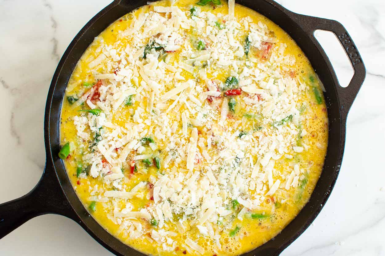 Uncooked frittata with parmesan cheese in a cast iron skillet.