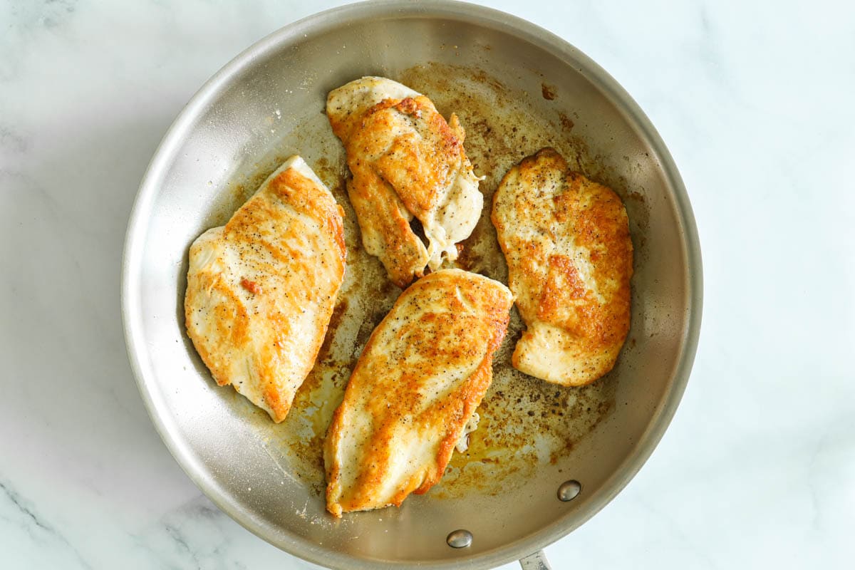 Four cooked chicken breasts in a skillet.