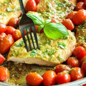 Pesto chicken breast on a fork, grape tomatoes around and fresh basil as garnish.