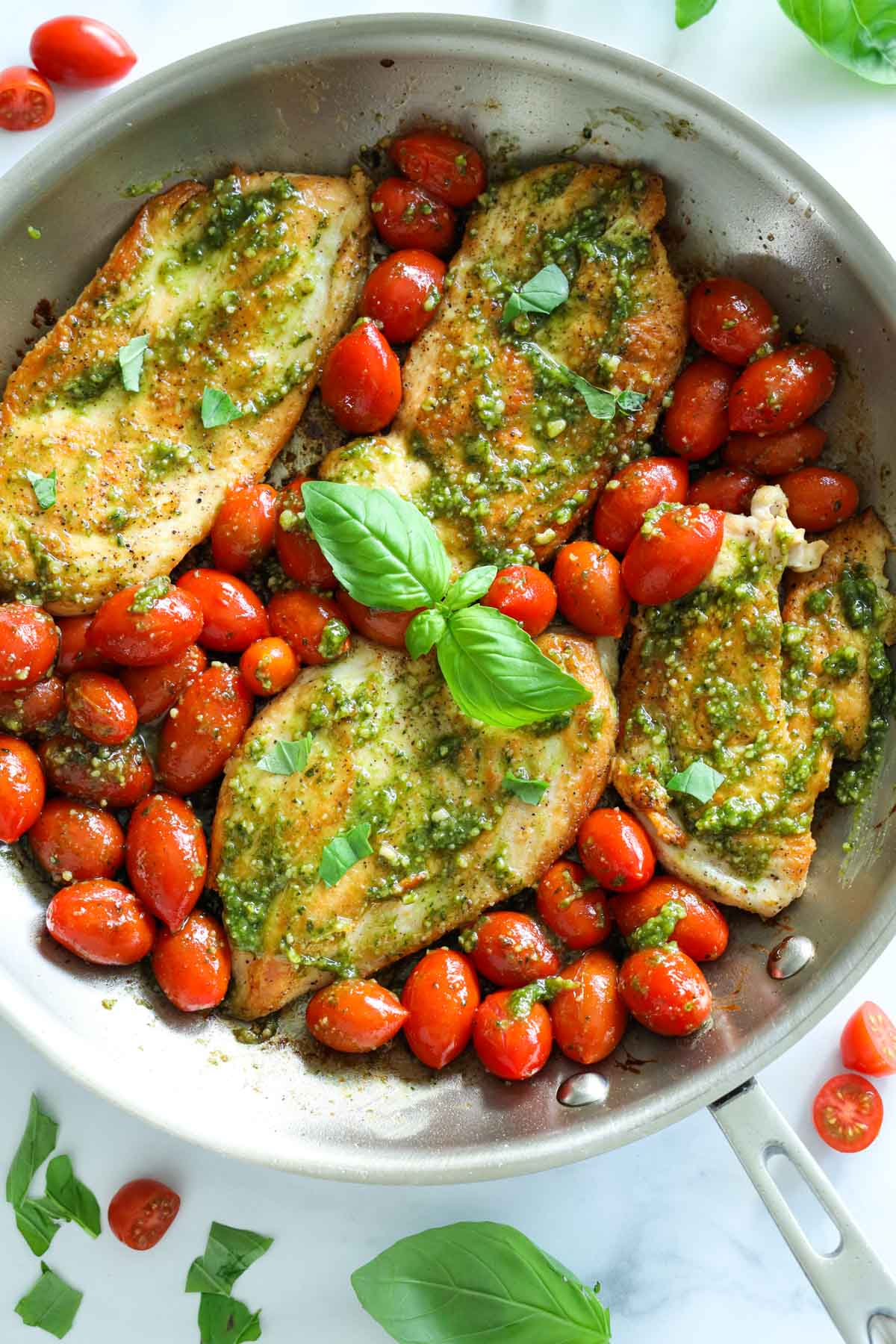 Pesto chicken with cherry tomatoes and basil in a pan.
