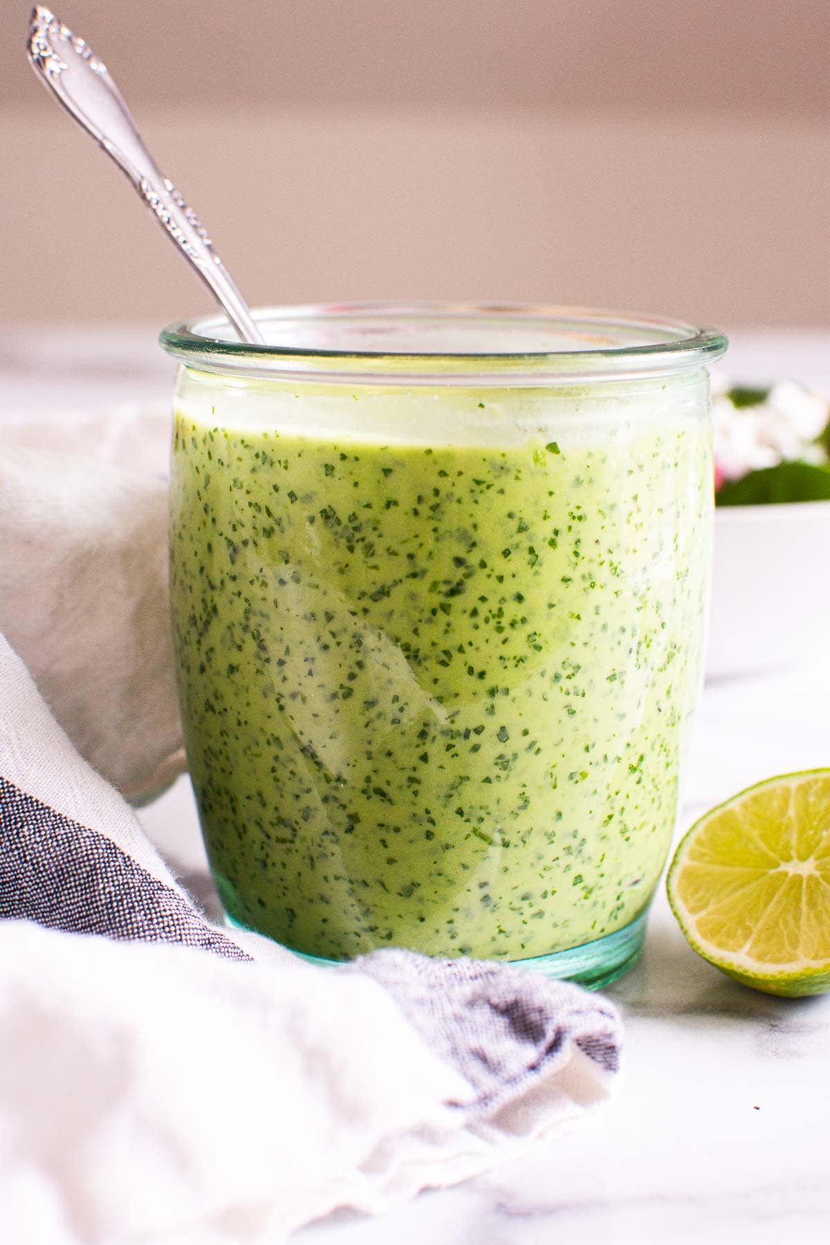 Avocado lime dressing in a glass jar with a spoon and cut up lime near it.