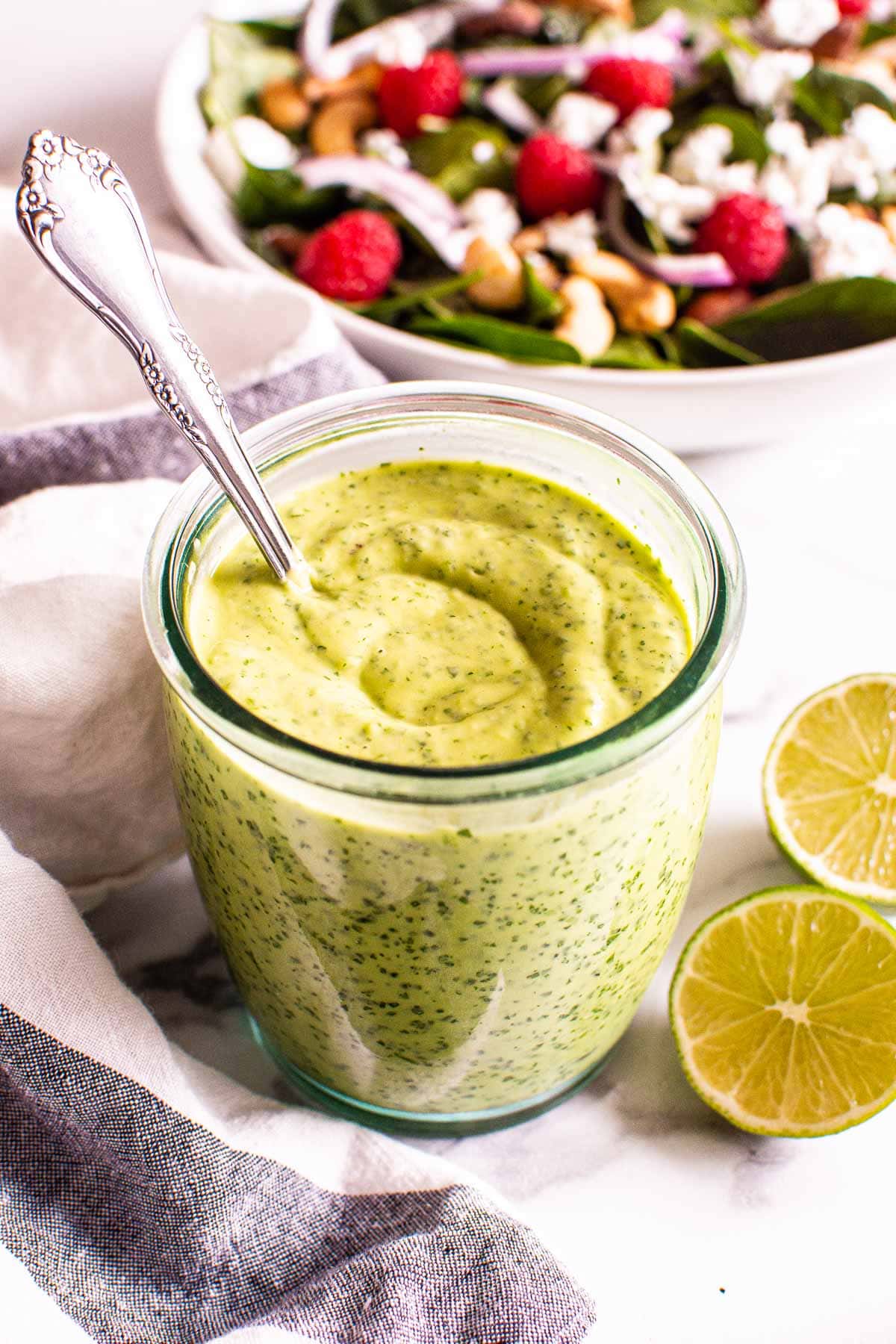 Avocado cilantro lime dressing in a glass jar and a bowl of salad on a counter.