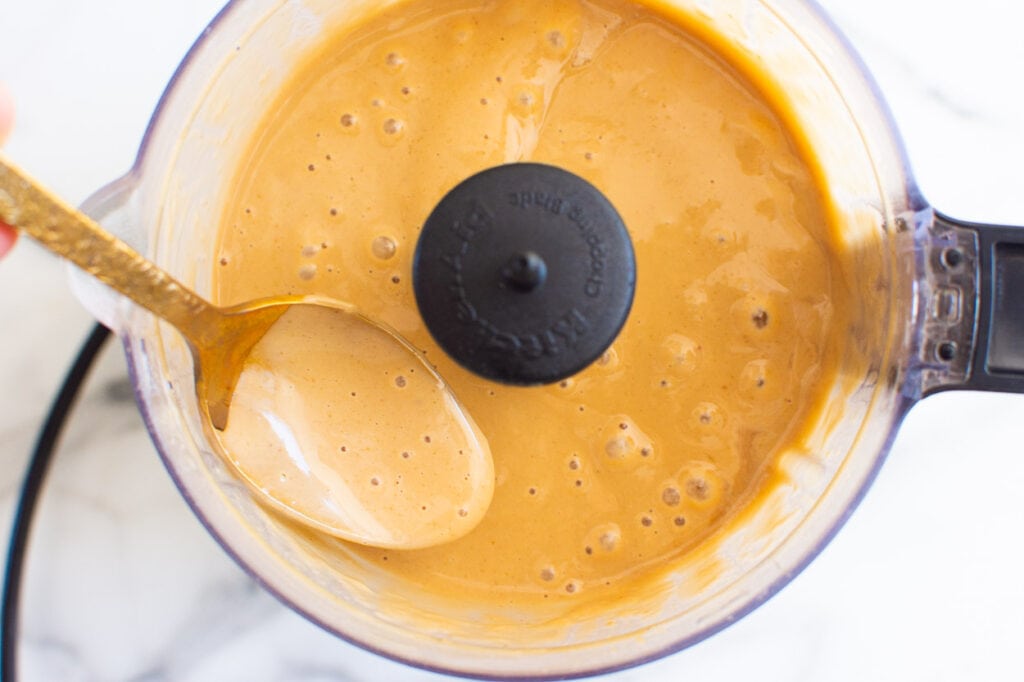 Creamy peanut sauce in food processor dripping of gold spoon.