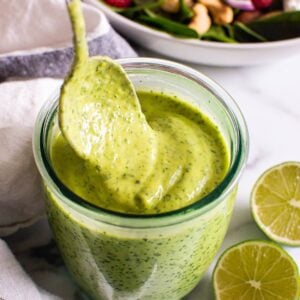 Avocado cilantro dressing dripping off a spoon into a glass jar.