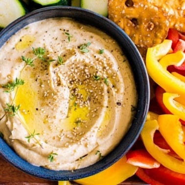garlic hummus in bowl with sliced vegetables
