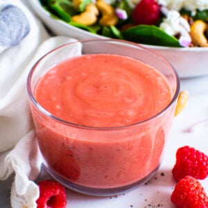 Raspberry vinaigrette dressing in a bowl with salad in the background.