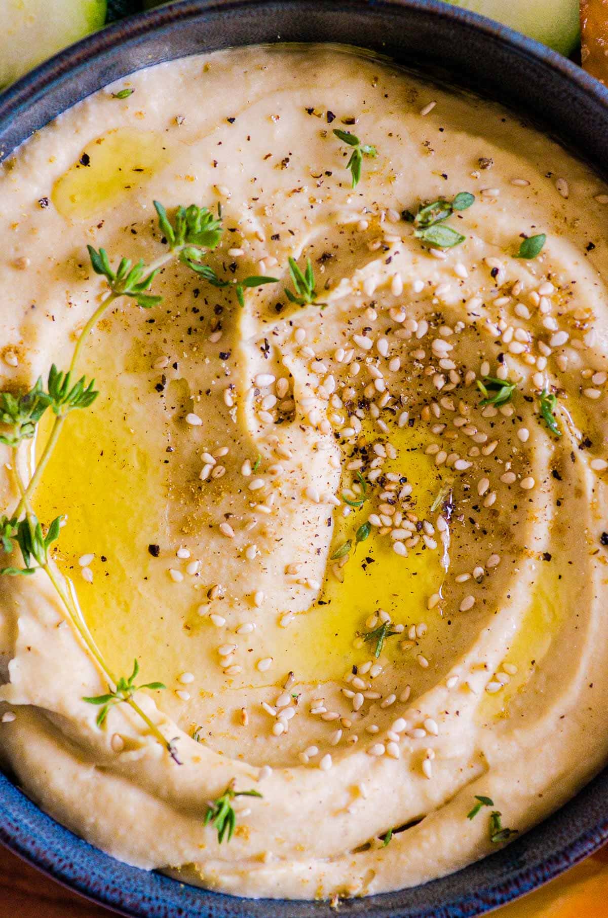 garlic hummus in bowl with olive oil and garnishes