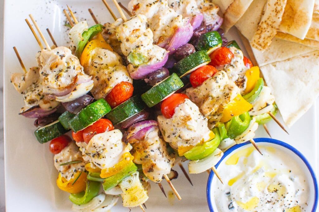 greek chicken kabobs on plate with sauce and pita