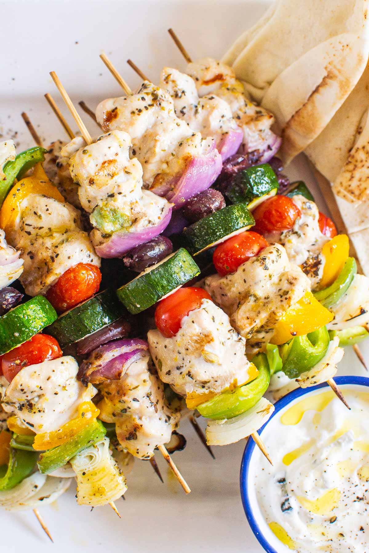 Greek chicken kabobs on skewers with sauce and pita on the side.