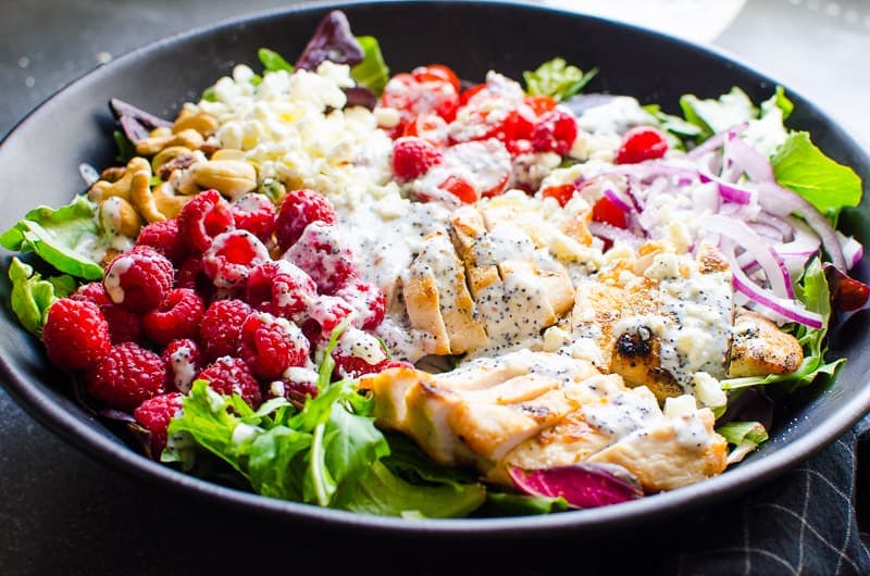 Grilled chicken breast sliced on salad with poppy seed dressing, berries, cashews, and onion.