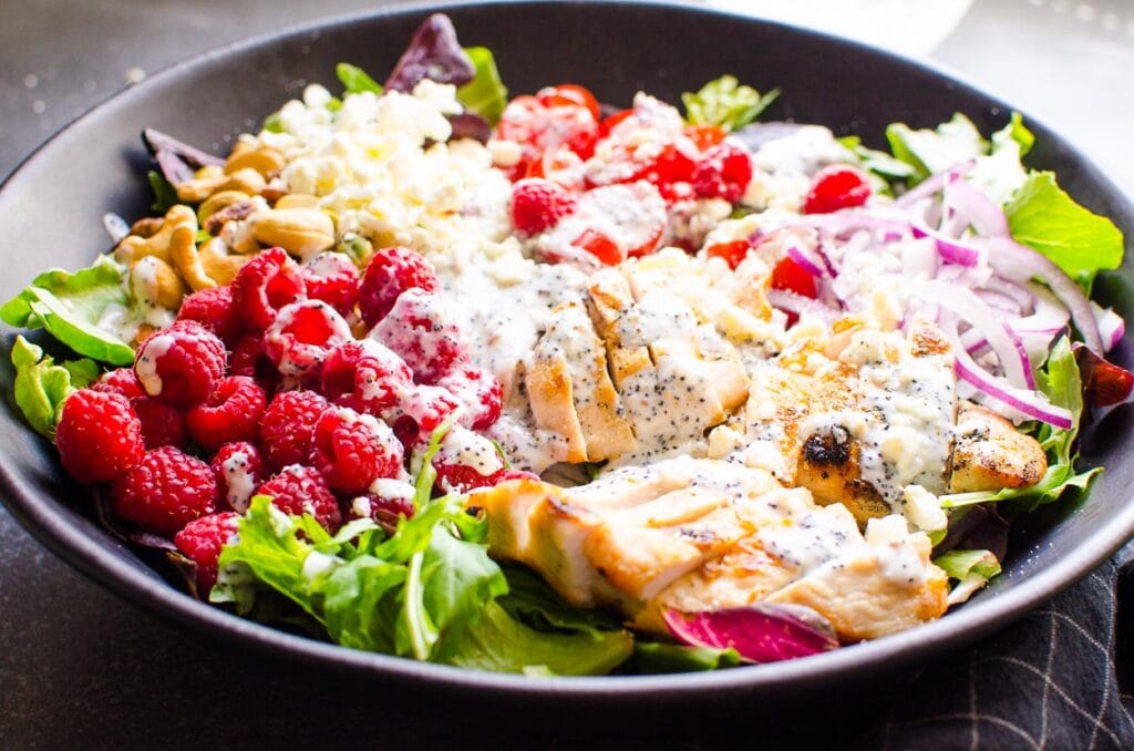 grilled chicken in a salad with dressing and raspberries