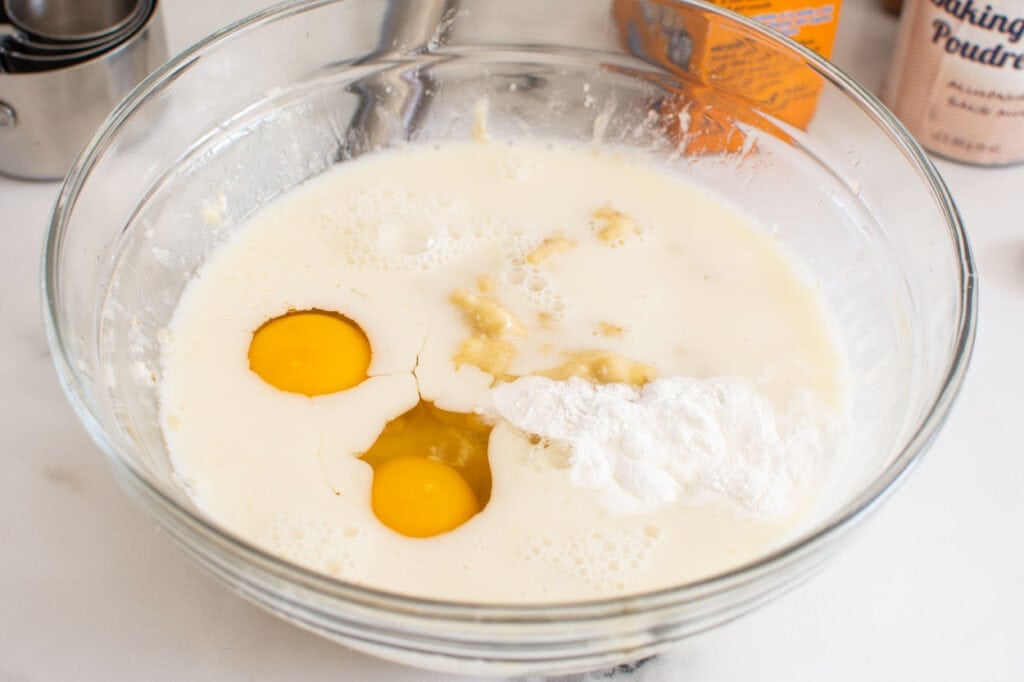 Milk, eggs, mashed banana, baking ingredients in bowl. 