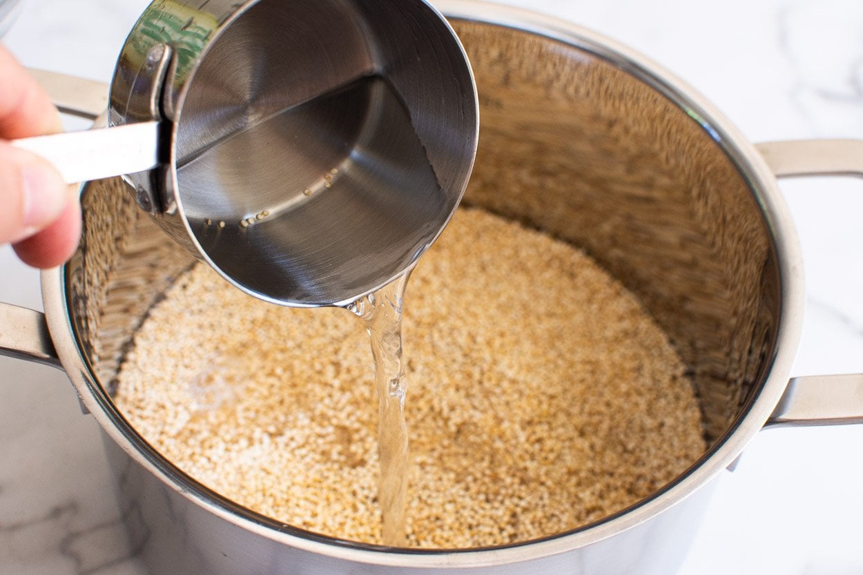 Adding water to uncooked quinoa in a pot.