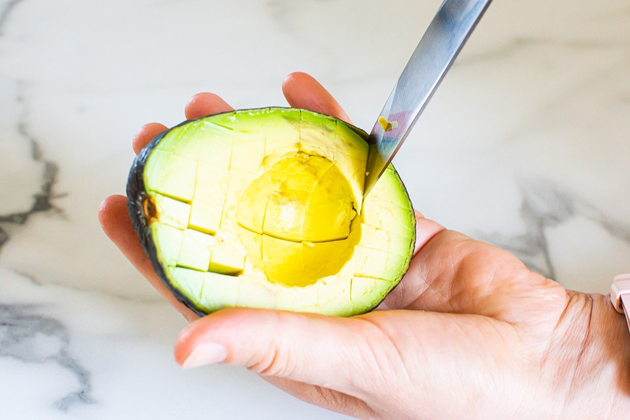 Person slicing avocado into cubes within its shell with a knife.