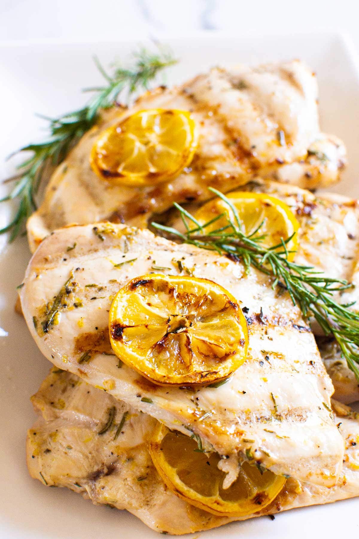 grilled lemon rosemary chicken breast in serving dish garnished with lemon and rosemary sprigs