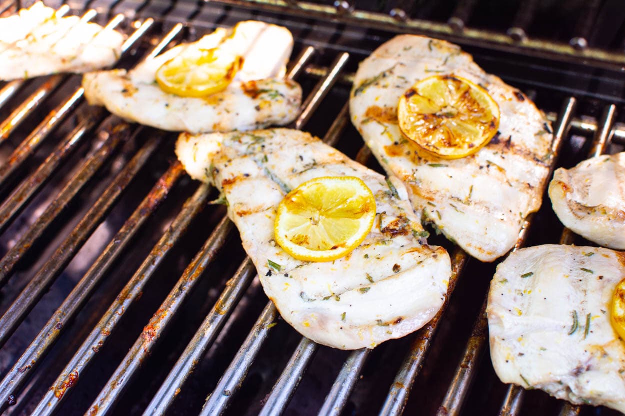 Grilled lemon rosemary chicken breasts with lemon slices on top on the grill.